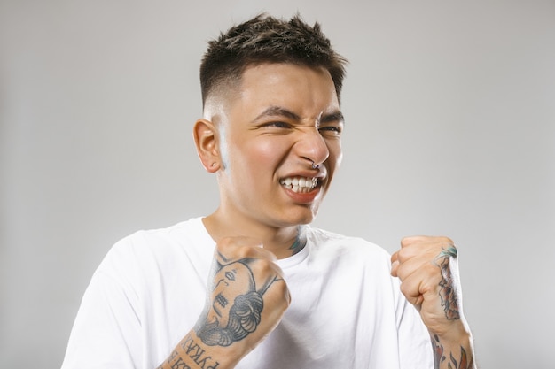 Free photo the young emotional angry man screaming on gray studio wall