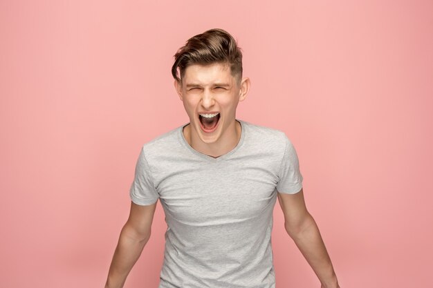 The young emotional angry man screaming on pink studio space