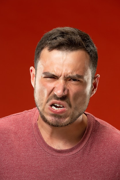 The young emotional angry man screaming on red studio wall