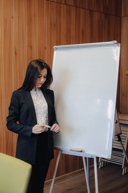 Young emotional attractive girl in business-style clothes working with flipchart in a modern office or audience