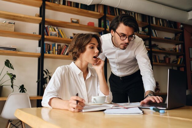 Young emotional business colleagues amazedly using laptop working on new project together in modern office