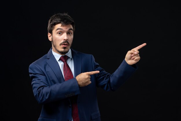 Young emotional concentrated man in suit pointing up on isolated dark wall