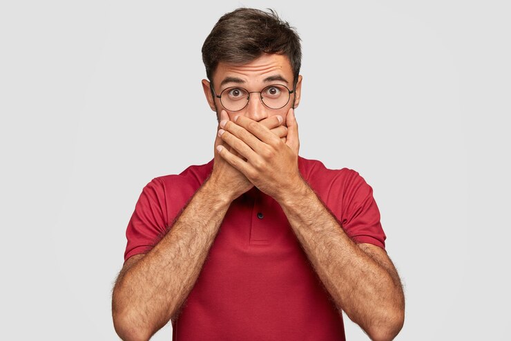 Free Photo young emotional man posing against the white wall covers mouth with hand