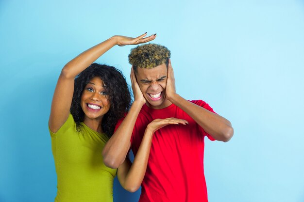 Young emotional man and woman in casual clothes posing on blue.