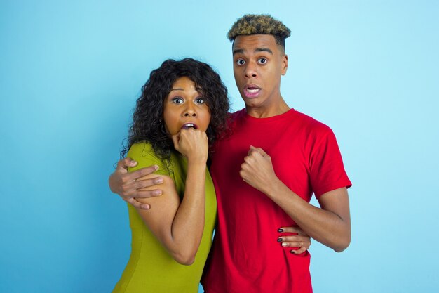 Young emotional man and woman in colorful clothes on blue.