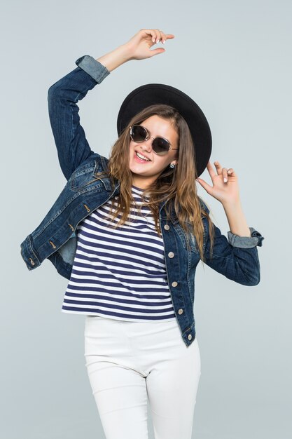 Young emotional woman in a black hat is dancing on white background