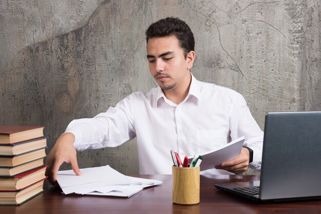 Young employee holding sheets of paper and sitting at the desk. High quality photo