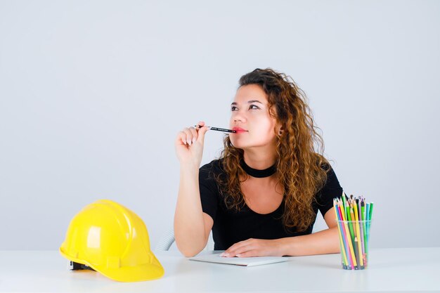 Young engineer girl is thinking by holding pencil on lips on white backgroundxDxA