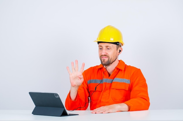 Young engineer is showing number four gesture by sitting in front of his tablet on white background