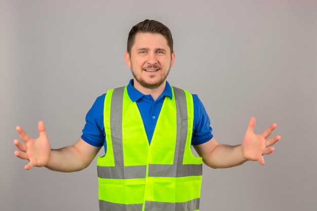Молодой инженер человек, одетый в строительный жилет, жестикулирующий руками, показывающими символ меры знака большого и большого размера, улыбаясь, глядя в камеру на изолированном белом фоне