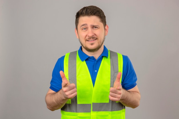 Foto gratuita giovane ingegnere uomo che indossa il giubbotto di costruzione guardando la fotocamera sorridente che punta con le dita alla fotocamera su sfondo bianco isolato