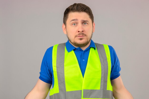 Young engineer man wearing construction vest looking confused having no idea what to do standing over isolated white background