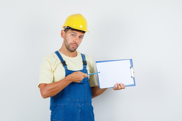 Young engineer in uniform pointing at clipboard , front view.