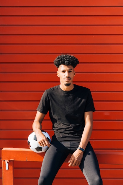 サッカーボールで座っている若い民族男