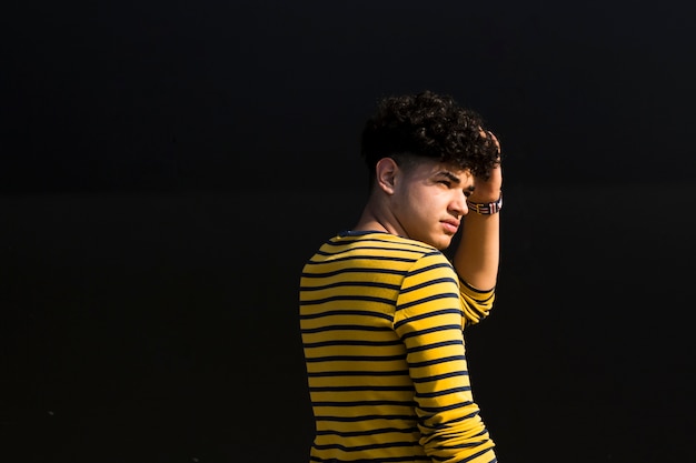 Young ethnic man with curly hair in striped shirt looking at light