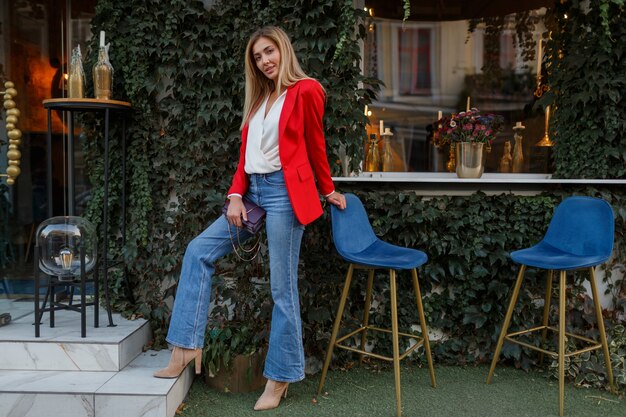 Young european  confident woman with   candid smile posing outdoor in the bar. Wearing red fashionable jacket