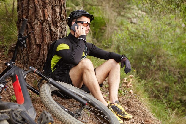 휴대 전화에 얘기하는 숲에서 쉬고 스포츠에서 젊은 유럽 사이클
