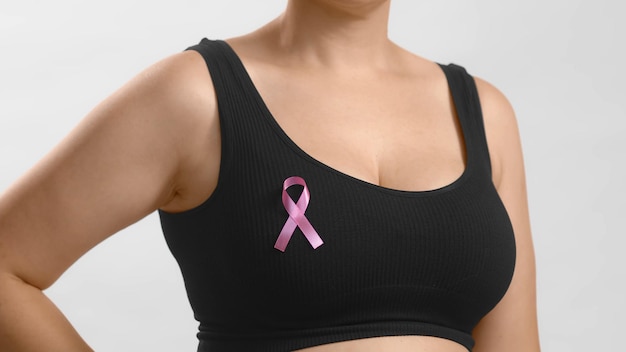 Free photo young european lady in a black top standing with a ribbon sign on her chest to support pink october and females combating breast cancer anonymous studio shot high quality photo on white background