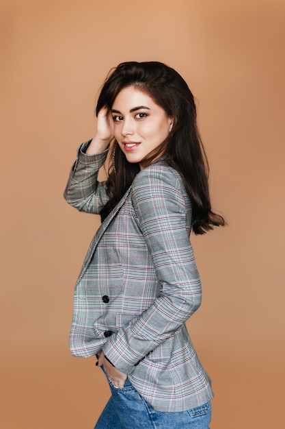 청바지와 격자 무늬 재킷에 젊은 유럽 여자 베이지 색 벽에 초상화에 대 한 포즈.