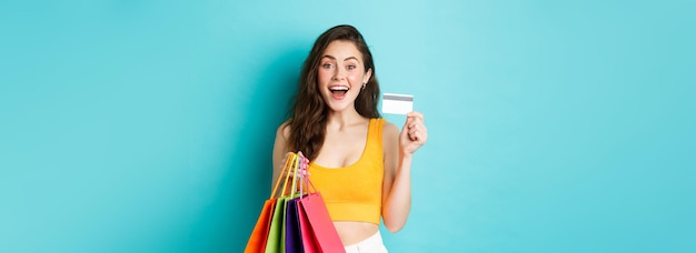 Foto gratuita giovane donna eccitata che tiene le borse della spesa e mostra le cose di acquisto di carte di credito in plastica durante il promo