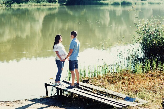 Young expecting couple stands on the bridge by the green river 