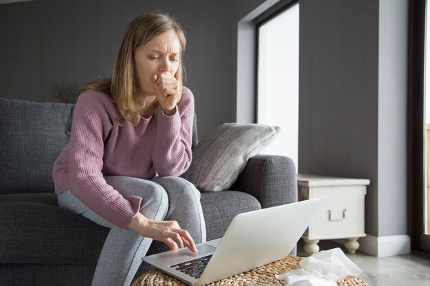 Young fair-haired woman yawning, typing on laptop with one hand