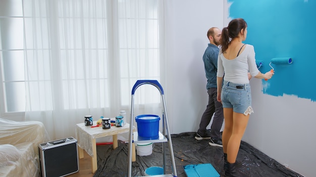 Young family painting apartment wall while redecorating with roller brush. Apartment redecoration and home construction while renovating and improving. Repair and decorating.