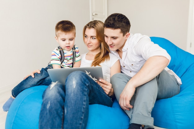 Young family of two parents and one boy child sit on blue sack chairs.