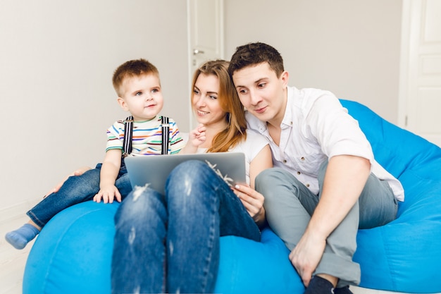 2人の両親と1人の男の子の子供の若い家族は青い袋の椅子に座っています。