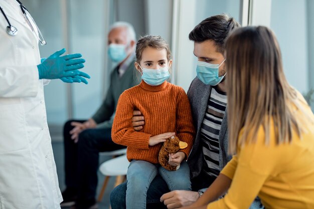 병원 대기실에 있는 동안 보호용 안면 마스크를 쓴 젊은 가족