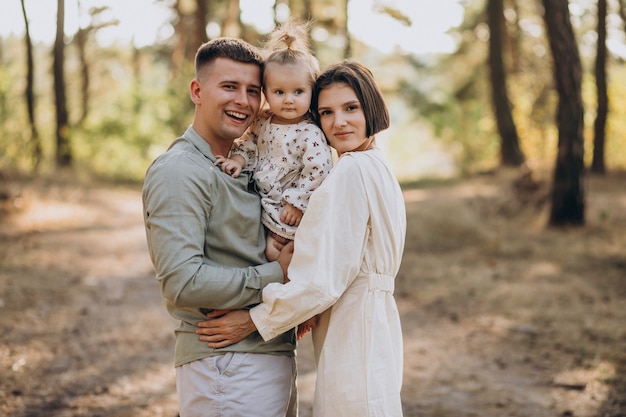 Young family with cute little daughter walking in forest on the sunset