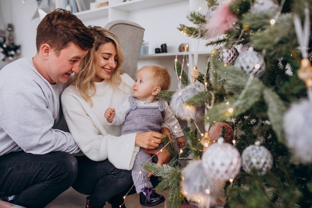 Young family with little daughter hanging toys on Christmas tree
