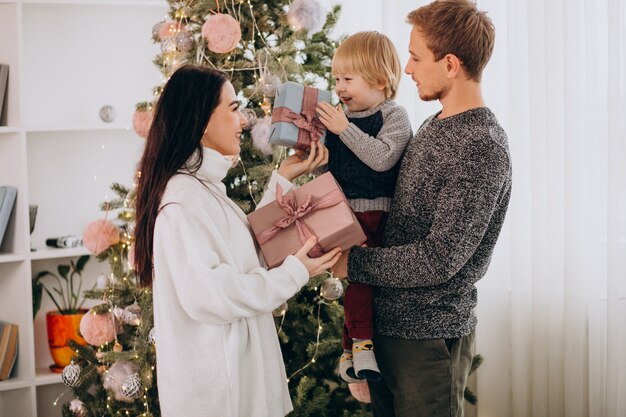 Молодая семья с маленьким сыном у елки держит рождественские подарки