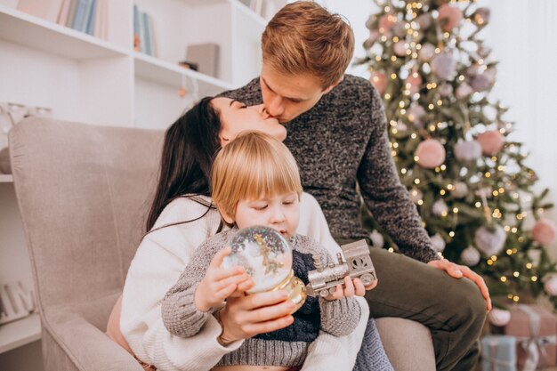 Young family with little son sitting by Christmas tree unpacking gifts