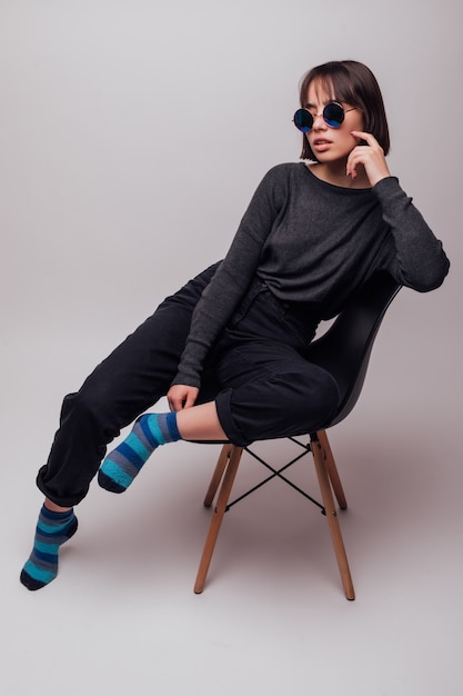 Young fashion beautiful woman in sunglasses sitting on chair isolated