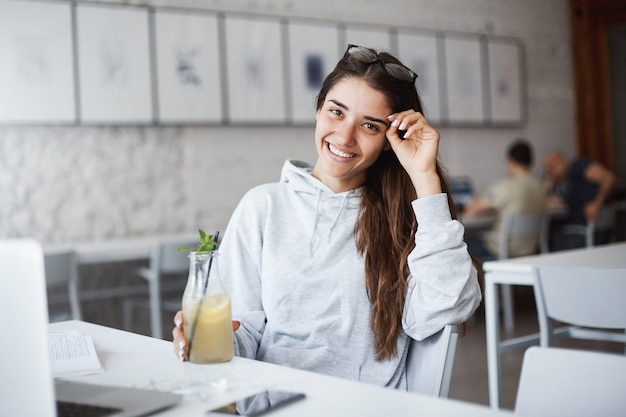 Young fashion design professional taking a break from her hard work drinking lemonade smiling listening to music in spacious open space coworking centre.