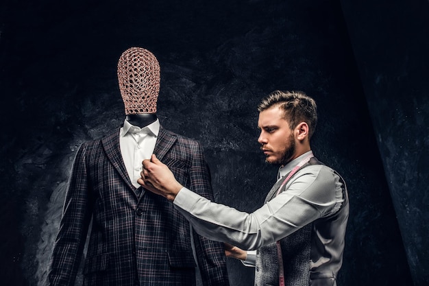 Молодой модельер проверяет качество сшитого на заказ элегантного мужского костюма в темной ателье