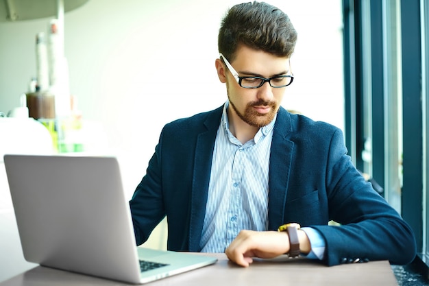 Young fashion smiling hipster man  in the city cafe during lunch time with notebook in suit looking at watches