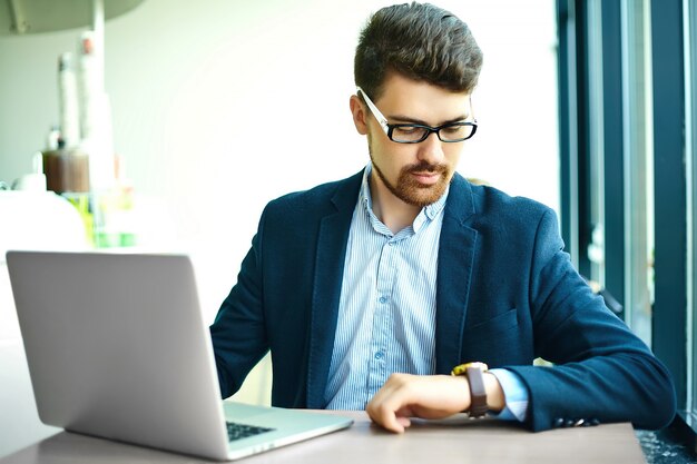 Young fashion smiling hipster man  in the city cafe during lunch time with notebook in suit looking at watches