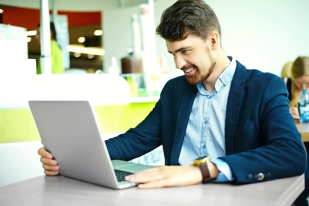 Young fashion smiling hipster man  in the city cafe during lunch time with notebook in suit