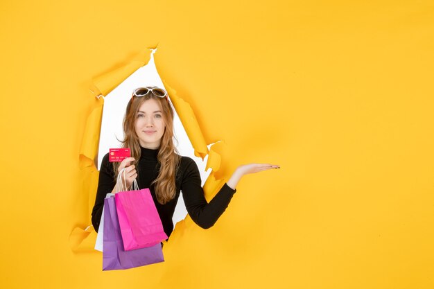 Young fashion woman holding shopping bags and credit card through torn paper hole in the wall