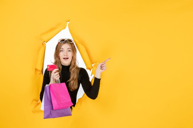 Young fashion woman holding shopping bags and credit card through torn paper hole in the wall