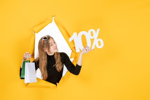 Young fashion woman holding shopping bags and discount percentage through torn paper hole in the wall