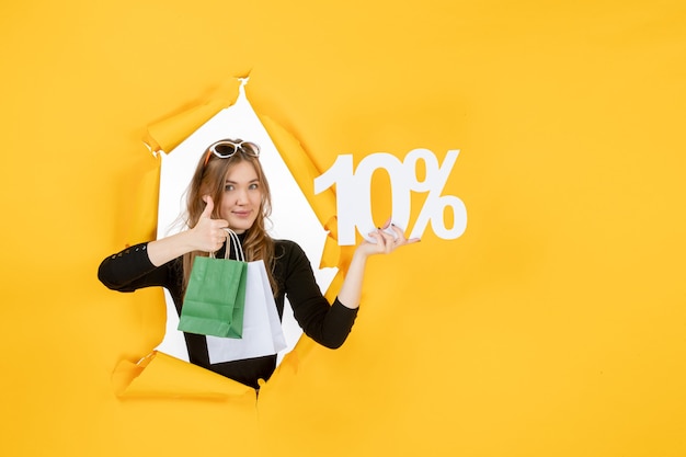 Free photo young fashion woman holding shopping bags and discount percentage through torn paper hole in the wall