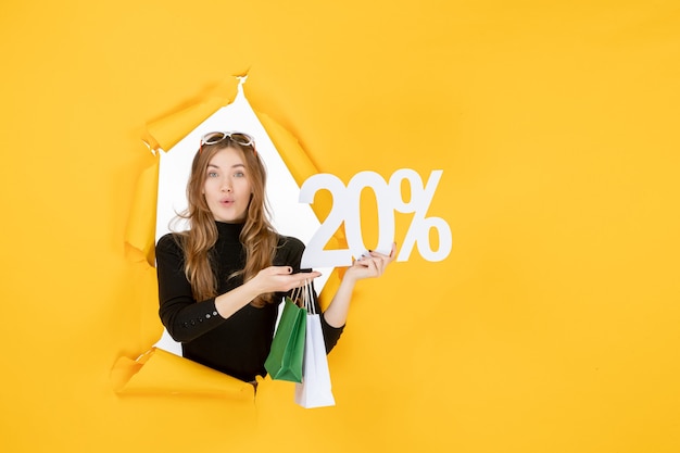 Young fashion woman holding shopping bags and discount percentage through torn paper hole in the wall