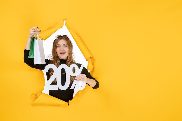 Free Photo young fashion woman holding shopping bags and discount percentage through torn paper hole in the wall
