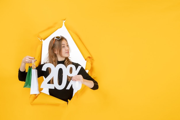 Young fashion woman holding shopping bags and discount percentage through torn paper hole in the wall