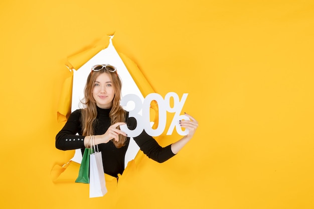 Young fashion woman holding shopping bags and discount percentage through torn paper hole in the wall