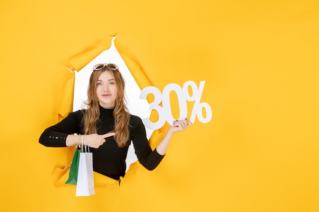 Young fashion woman holding shopping bags and discount percentage through torn paper hole in the wall