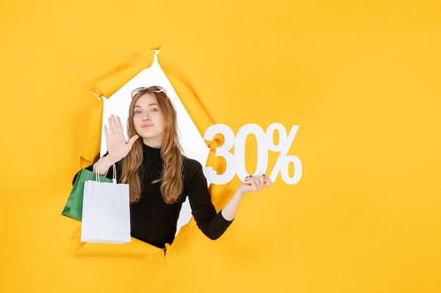 Free photo young fashion woman holding shopping bags and discount percentage through torn paper hole in the wall